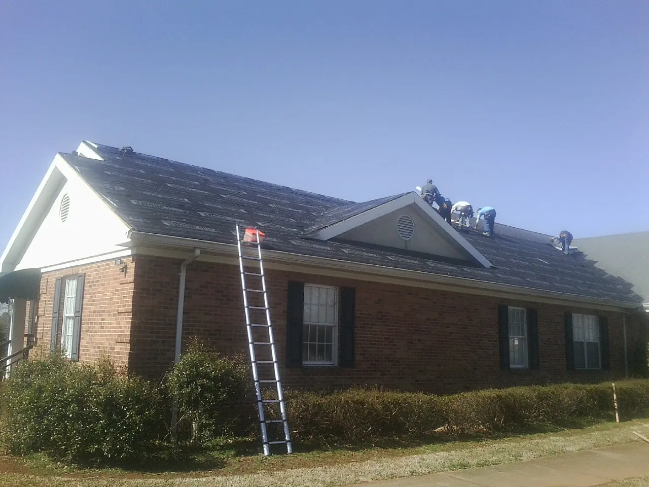 Crew tearing shingles off a brick ranch roof with a ladder set — Emergency Roof Repair work by our crew in Gulfport