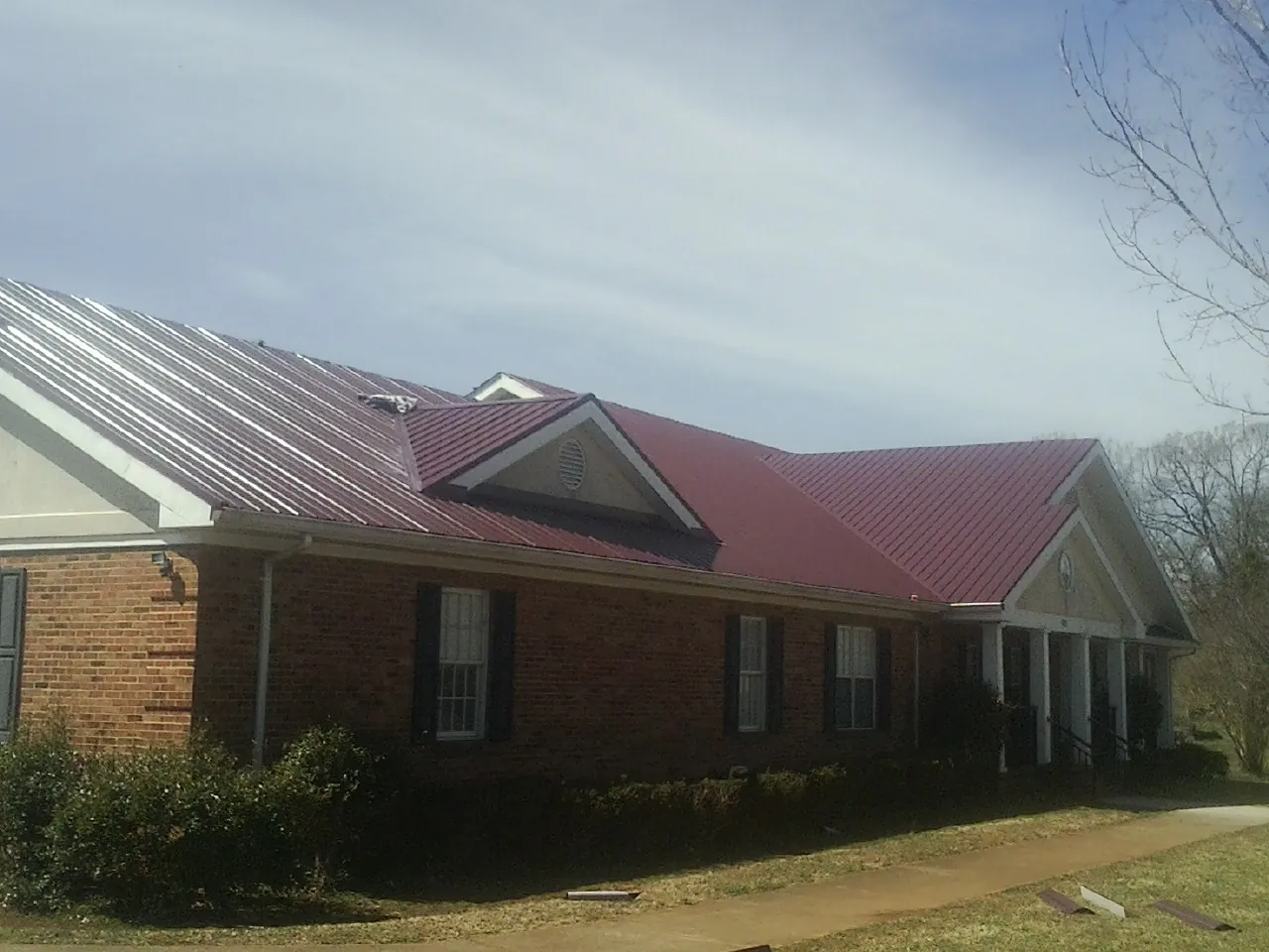 Red metal roof with gabled entries on a long brick building, from a Hail Damage Roof Repair job in Gulfport