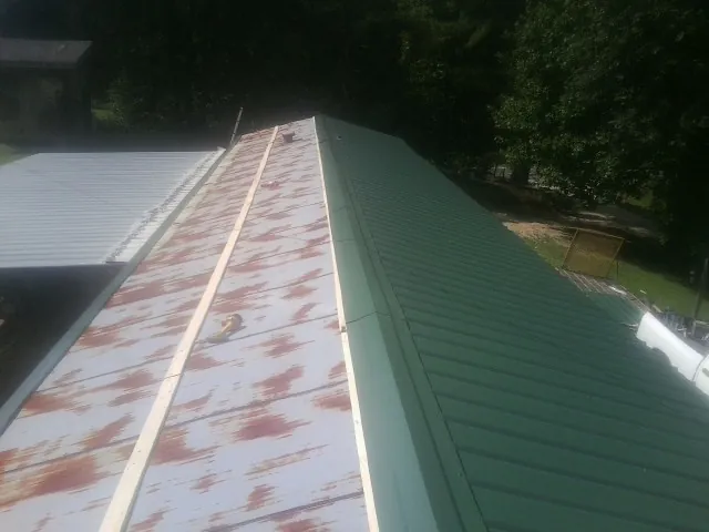 Old rusted panels beside newly installed green metal roofing — Wind Damage Roof Repair by Roofing Brothers in Gulfport