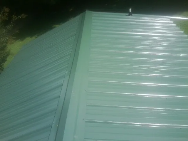 New green metal panels meeting at the ridge of a roof — Flat Roof Repair work by our crew in Gulfport