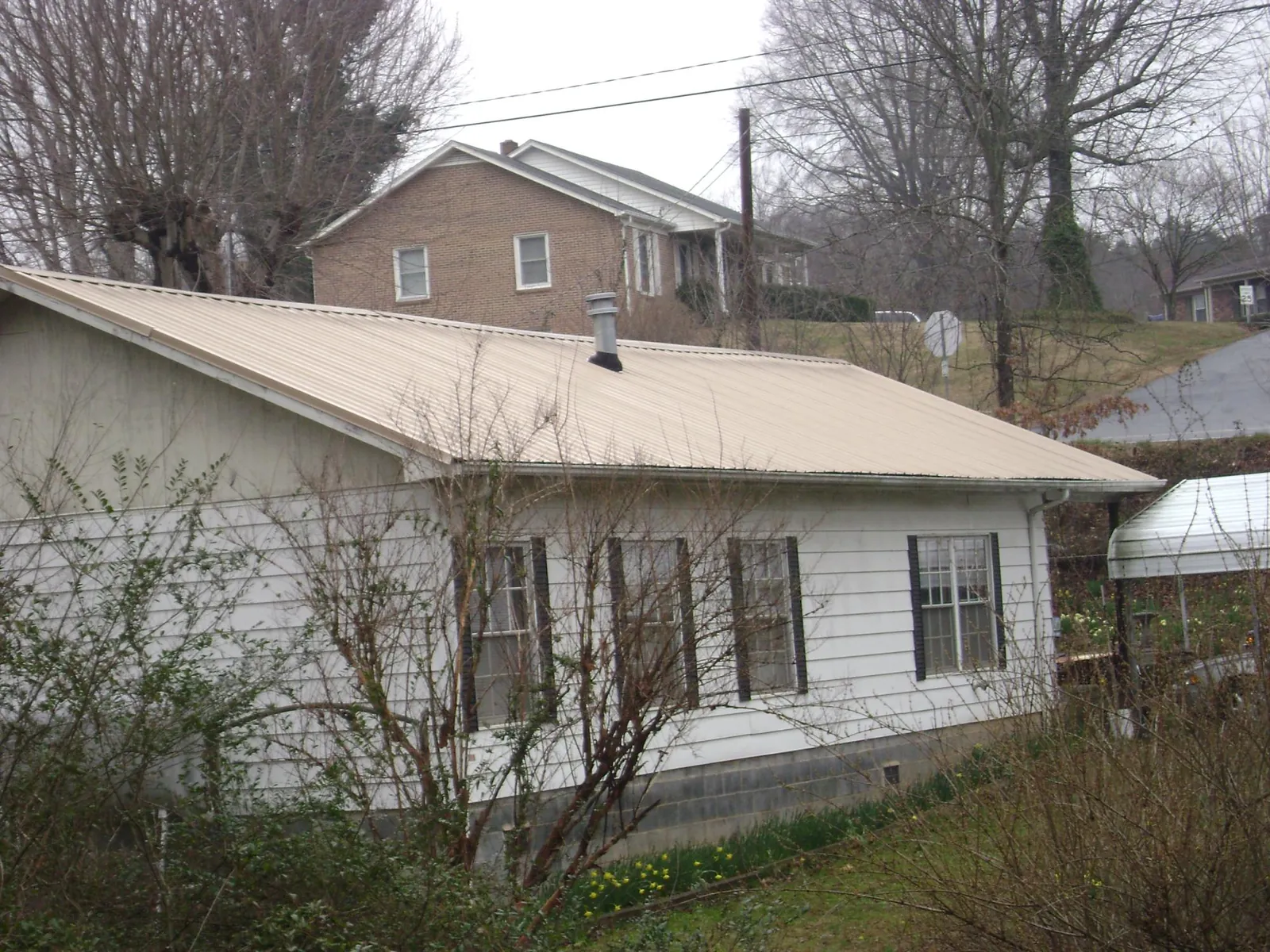 Tan metal roof on a white sided house set into a hillside — Commercial Roofing by Roofing Brothers in Gulfport