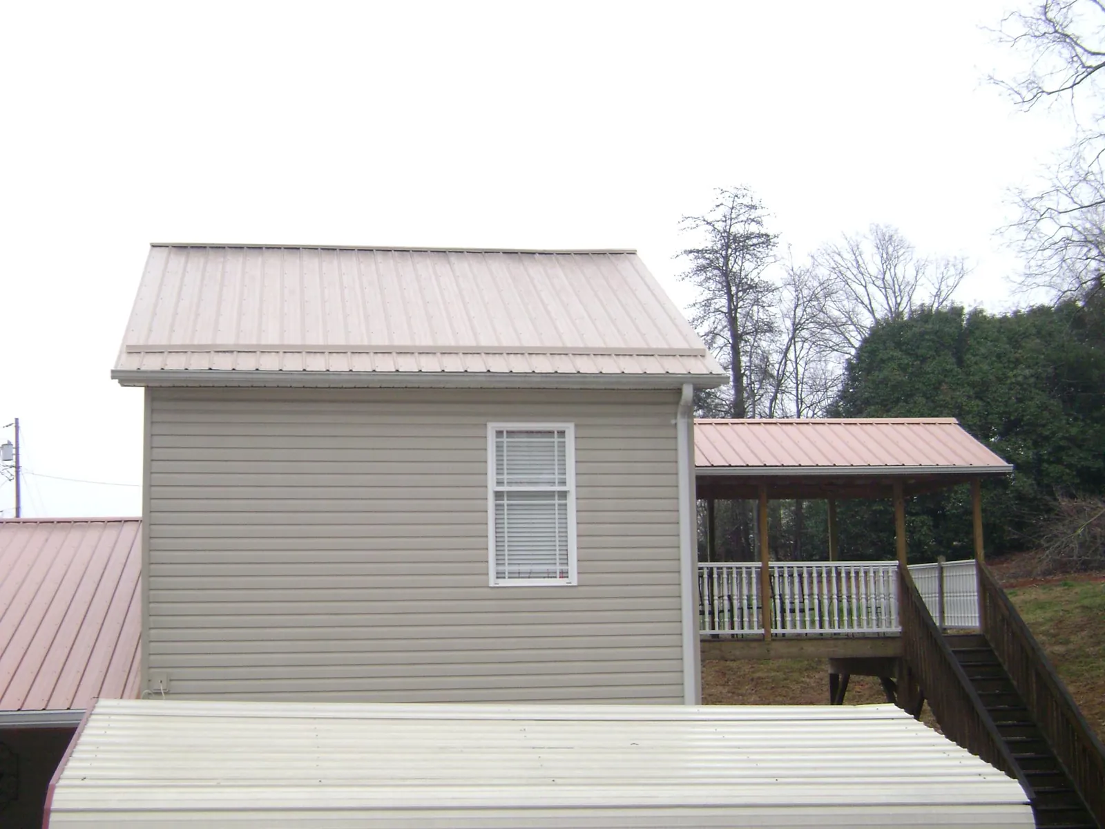 Tan metal roofs on a two story addition and attached porch, from a Roof Replacement job in Gulfport